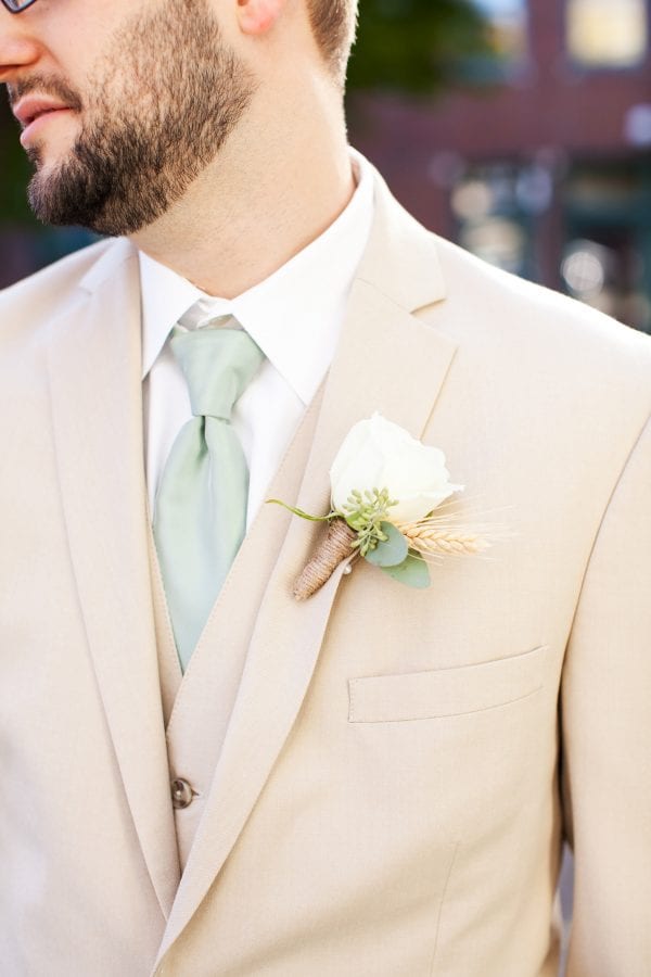 This tan suit looks great for a garden wedding in any season. The neutral tone allows for a wide range of complimentary colors like this sage tie and crisp white rose boutonniere. Image by Jen & Chris Creed