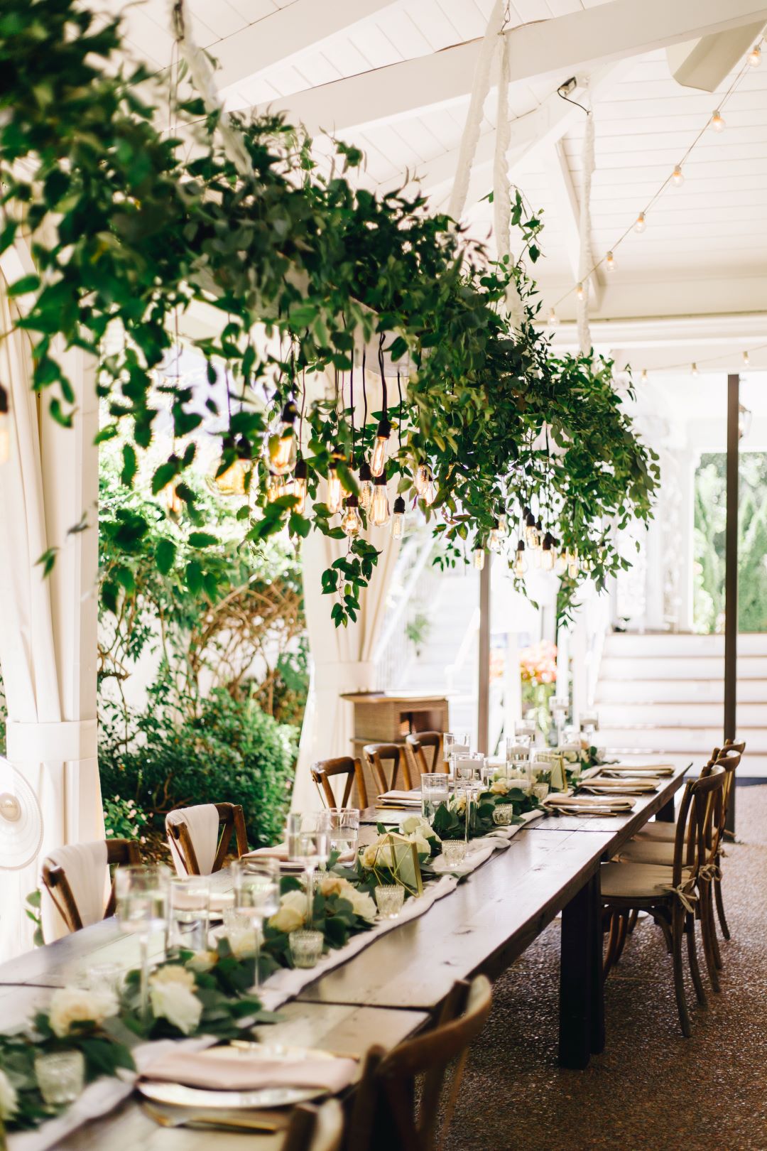 Long wedding party table with greenery hanging in chandeliers at earthy summer garden wedding in September, neutrals & greenery