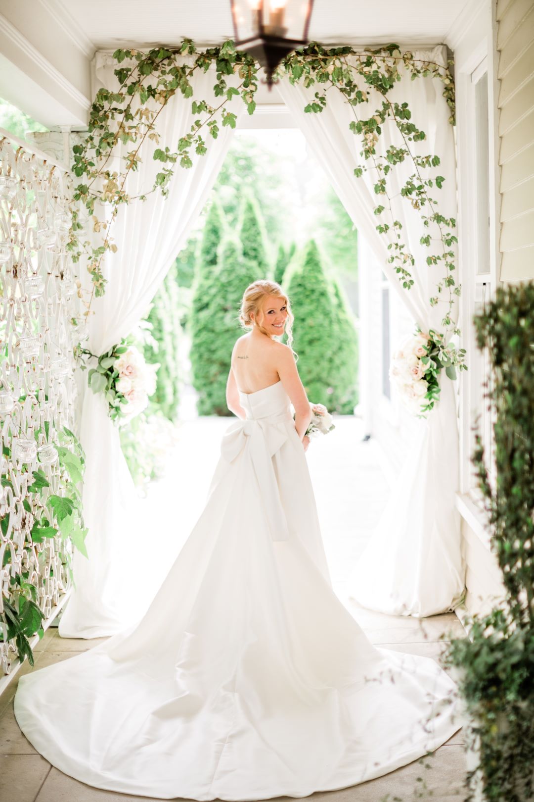 CJ's Off The Square | Bride posing in her wedding gown with a train under an arch of greenery