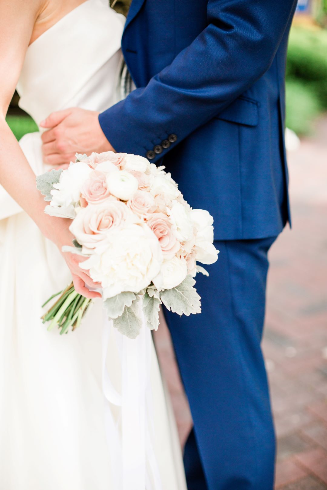 CJ's Off The Square | Close up of groom holding bride's waist and highlighting bouquet of blush roses