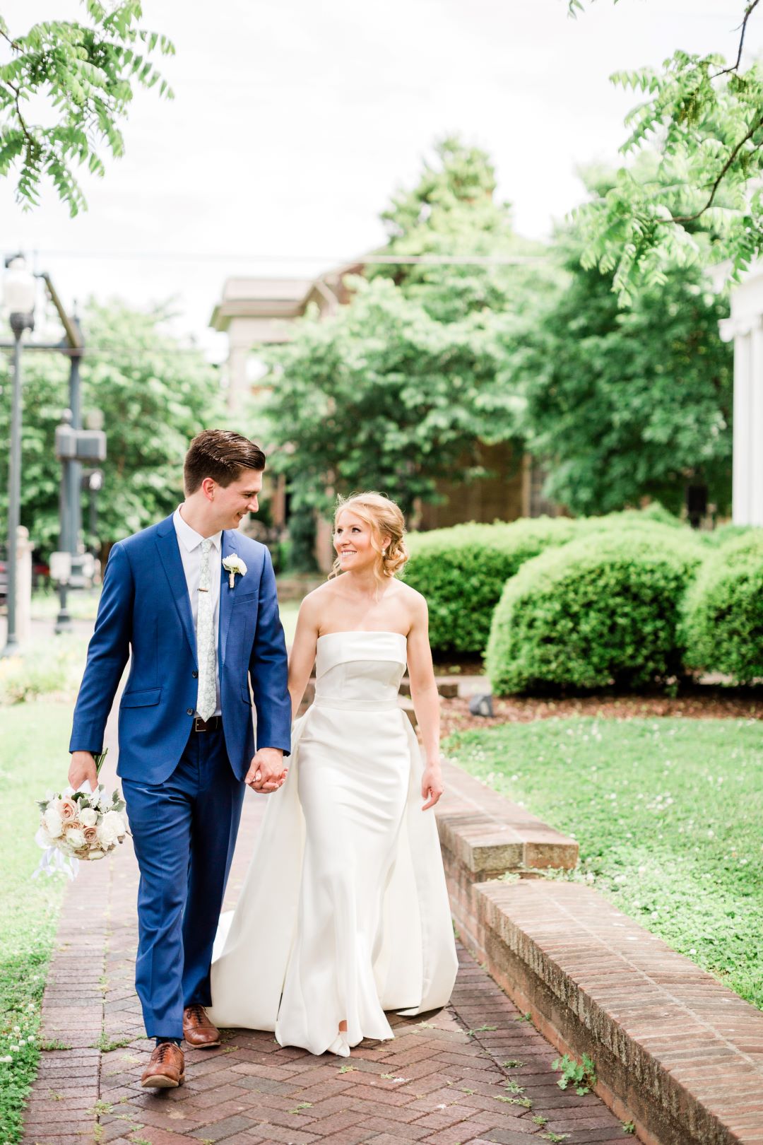 CJ's Off The Square | Bride and groom walking down brick walkway in front of lush greenery