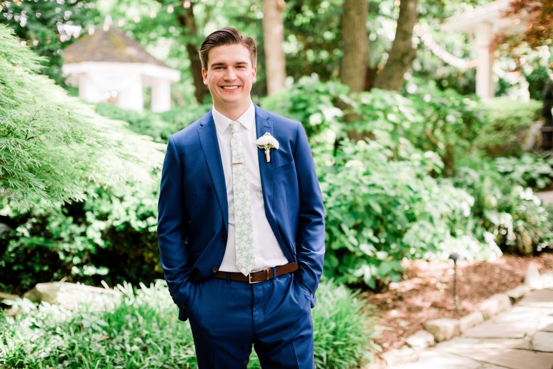 CJ's Off The Square | Groom in a cobalt blue tux and printed tie, smiling in the garden before his wedding