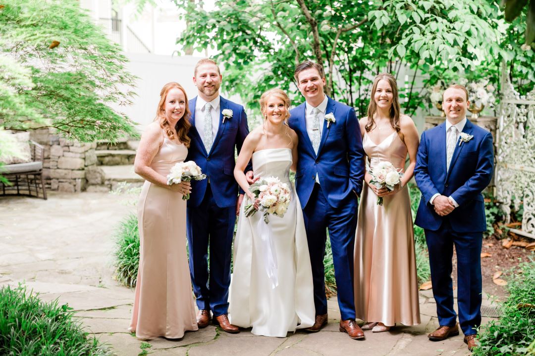CJ's Off The Square | Wedding party posing in the garden of the wedding venue in blue tuxedos and blush bridesmaids dresses