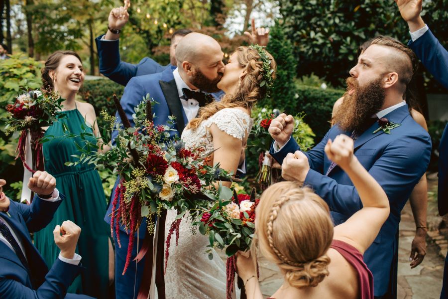 Bride and groom kissing with wedding party cheering them on / earthy / fall / October / burgundy
