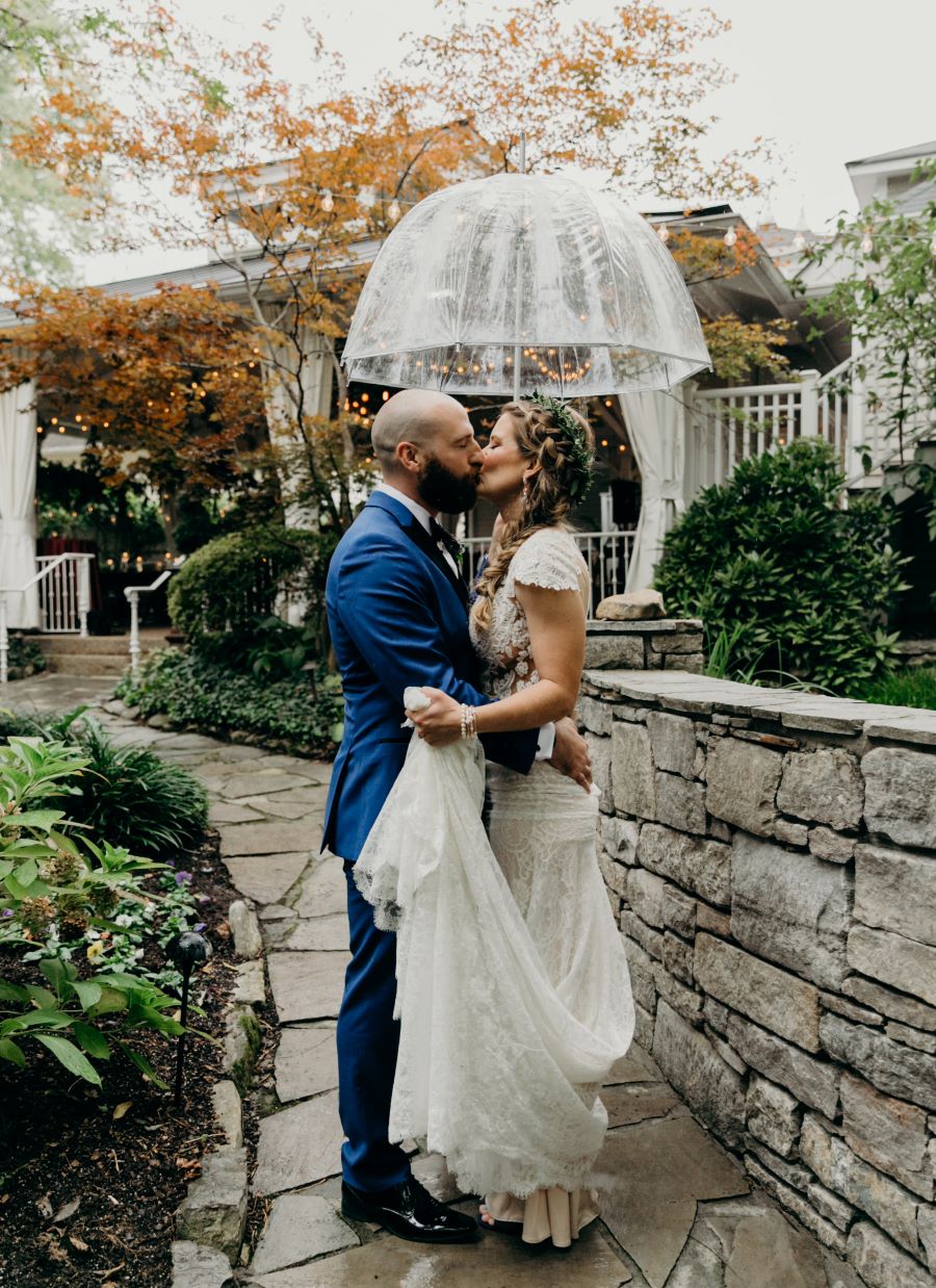 Bride and groom kissing under an umbrella on their rainy wedding day / earthy / fall / October / burgundy