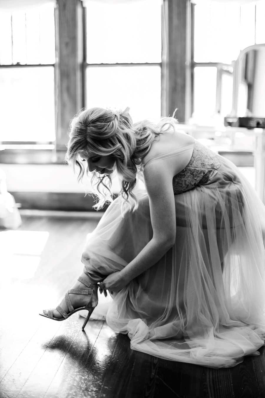 Bride putting shoes on in front of big window at CJ's Off the Square / Elopement / Spring / March / Dusty Rose