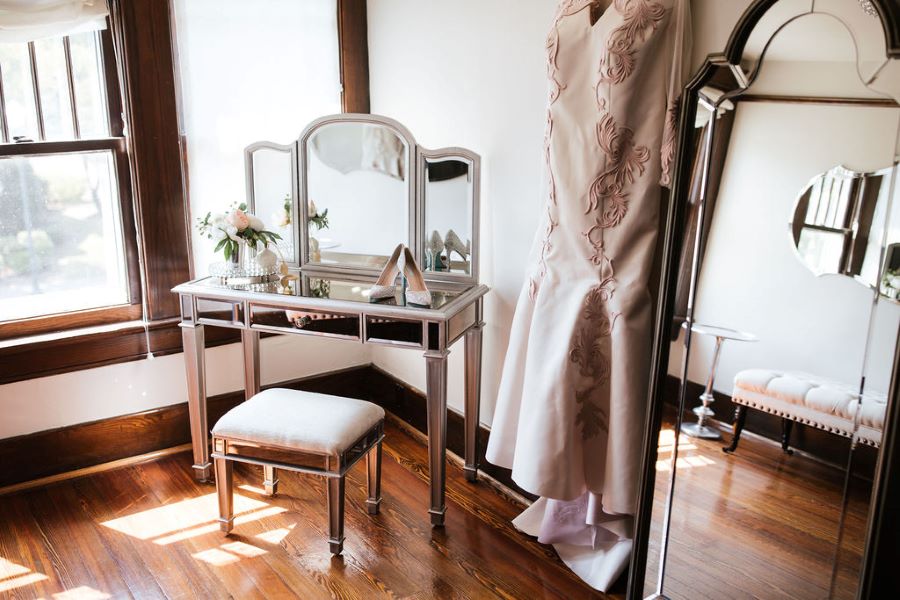Bride's trumpet dress hanging in dressing suite, shoes sitting on vanity / romantic lgbtq / fall / September / blush / burgundy