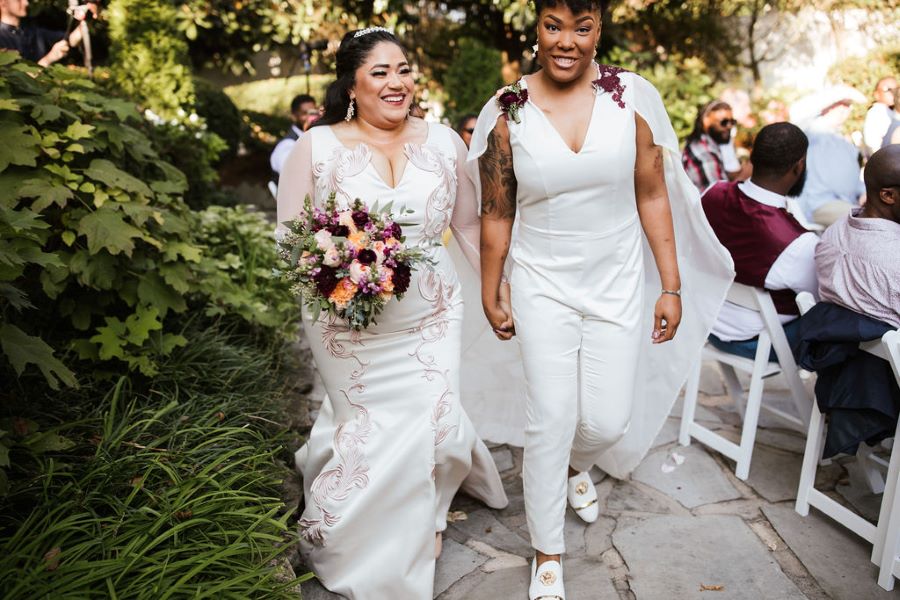 Brides holding hands and walking back up the aisle after being wed / romantic lgbtq / fall / September / blush / burgundy