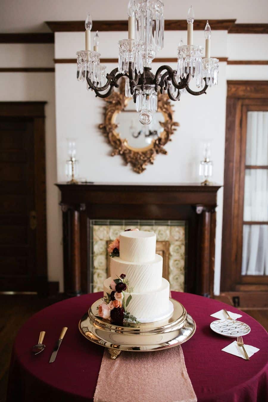 White wedding cake with blush, peach, and burgundy flowers under chandelier / romantic lgbtq / fall / September / blush / burgundy