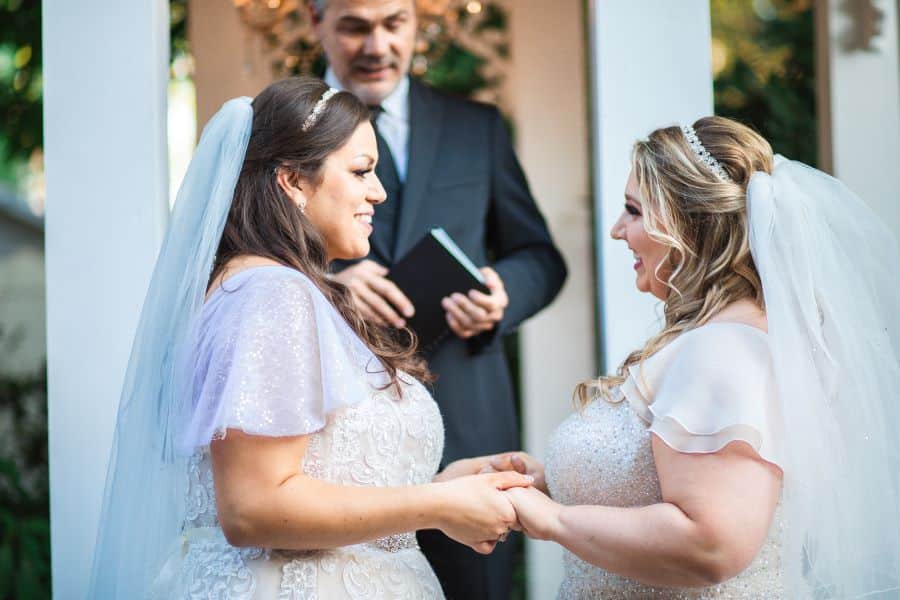Same sex brides smiling and holding hands in front of gazebo / Romantic / Summer / September / Pink / Dusty Rose / Cream