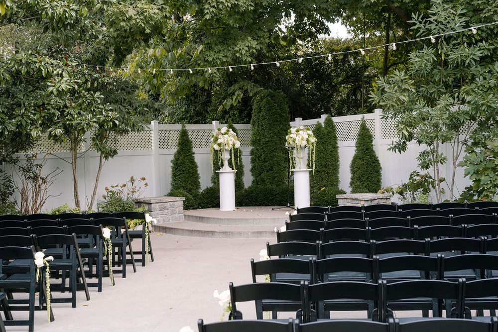 Garden wedding ceremony seating with black chairs and white floral arrangements