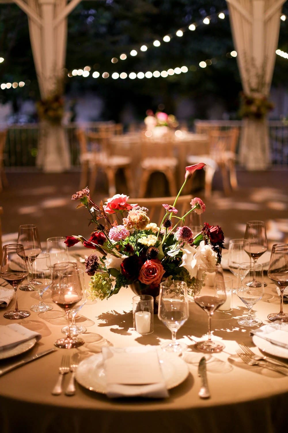 Romantic floral centerpiece and candlelit wedding table beneath string lights in Franklin Tennessee